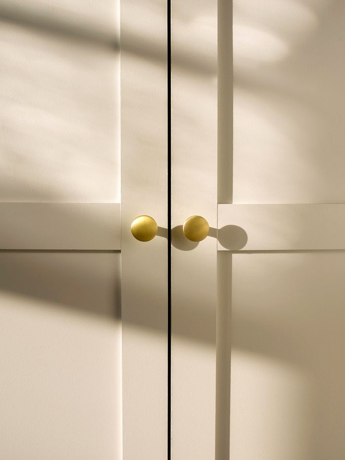 Minimalistic white doors featuring brass handles and natural shadows creating a serene atmosphere.